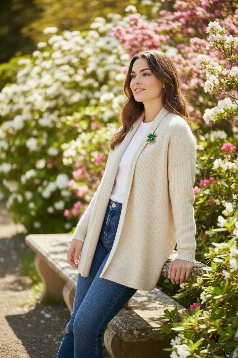 Luna Cotton four-leaf clover brooch with green crystals on a cream cardigan worn by a woman in a garden