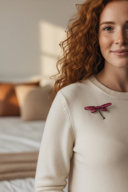 Luna Cotton dragonfly brooch with textured magenta wings and metallic body pinned to a woman's cream knit sweater
