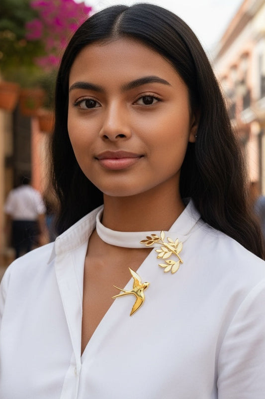 Luna Cotton gold swallow and olive branch collar brooch worn by a woman on a white shirt in a sunlit street