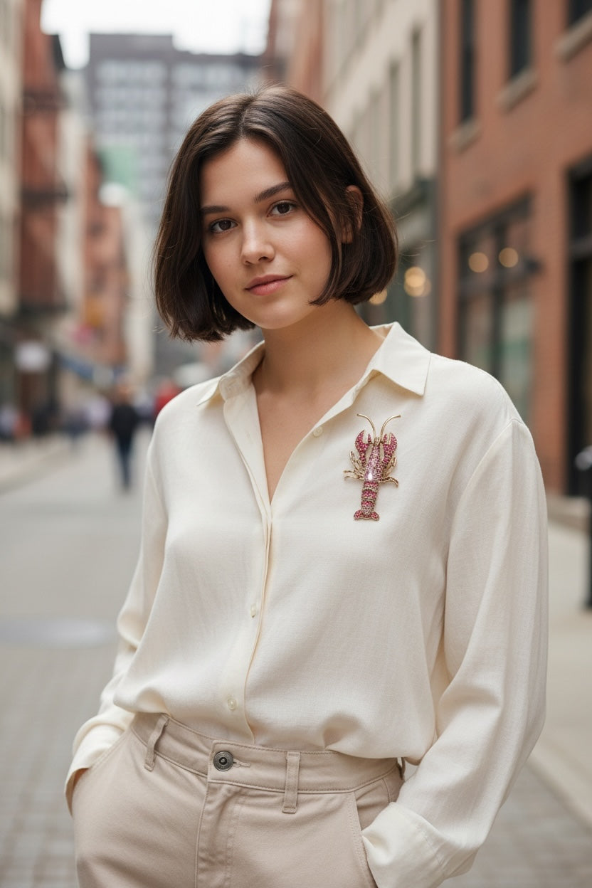 Luna Cotton lobster-shaped lapel pin brooch with pink crystals worn on a woman in a cream shirt on a city street