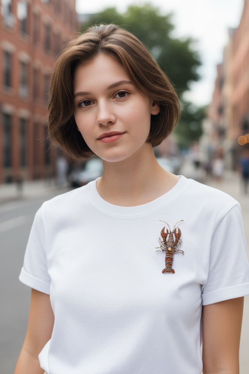 Luna Cotton crystal-embellished lobster brooch pinned to a woman wearing a simple white t-shirt on a city street.