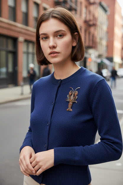 Luna Cotton crystal-embellished lobster brooch pinned to a navy blue cardigan worn by a woman on a city street