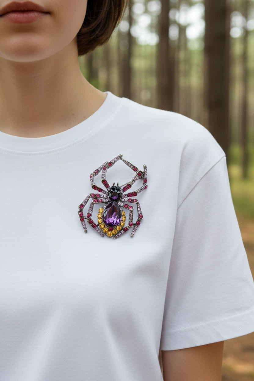 Luna Cotton spider brooch with purple teardrop crystal and pink, violet, and yellow stones on a white t-shirt